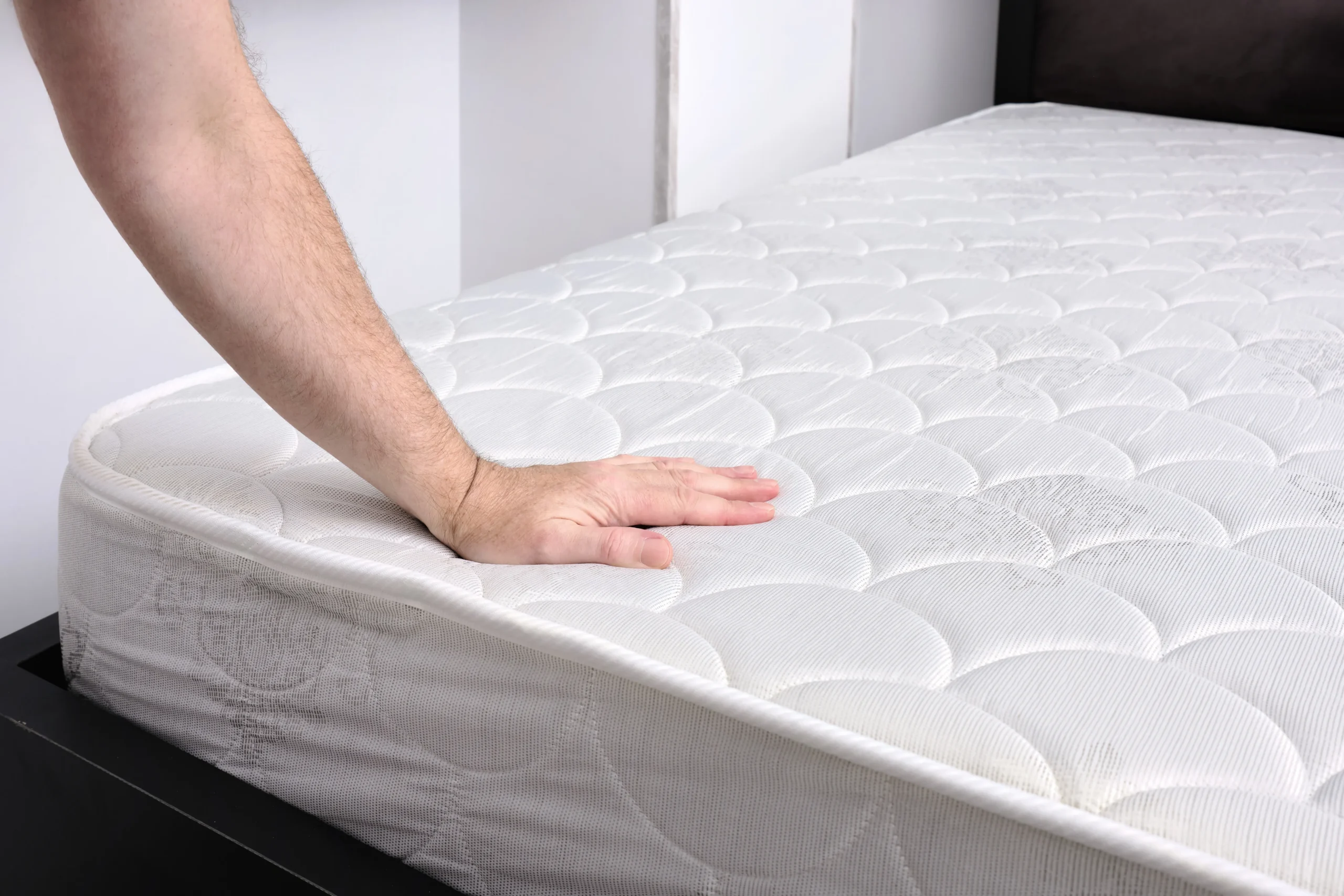 A person's hand pressing down on a white quilted mattress to inspect for a bed bug infestation.