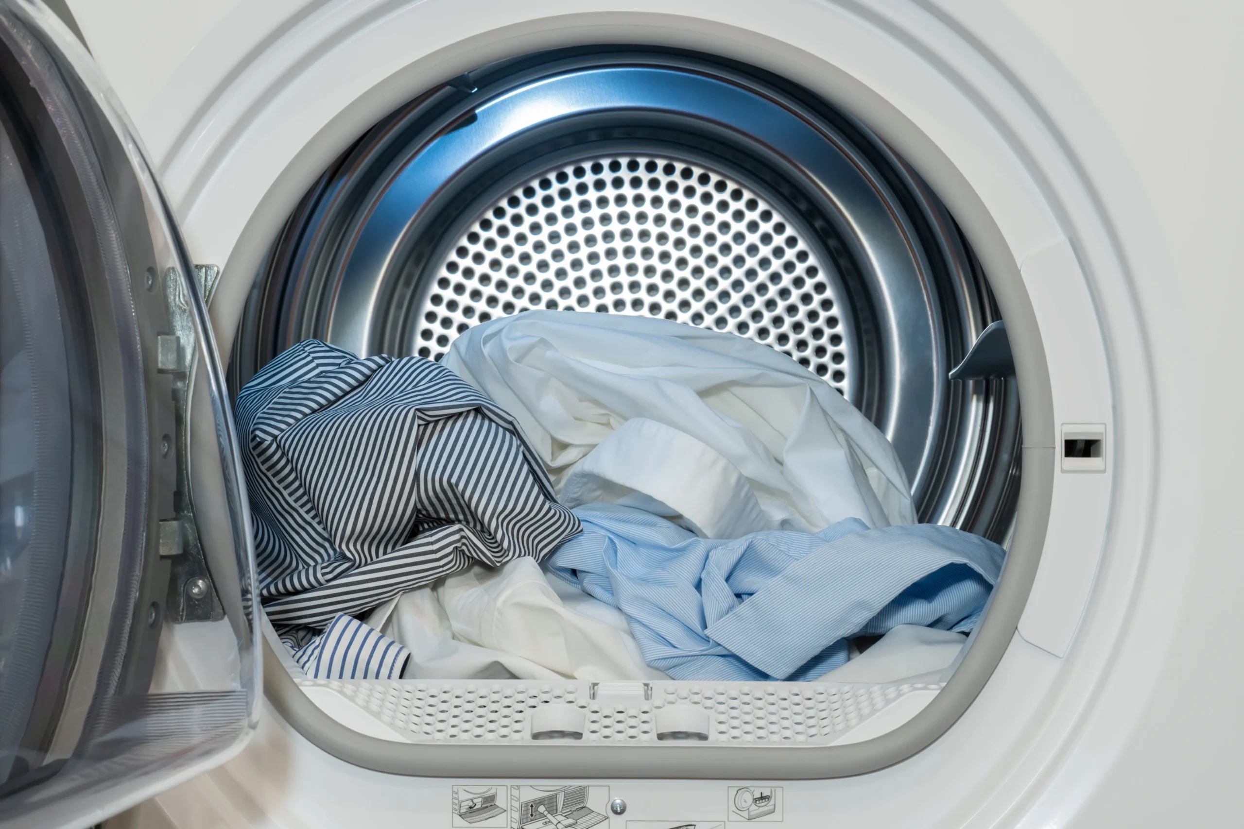 Bedding and clothing loaded into a washing machine dryer drum to kill bed bugs using high heat.