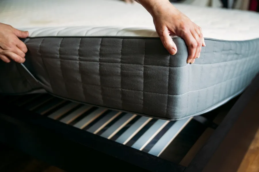 Person lifting a mattress to inspect the bed frame and prevent bed bugs from spreading.