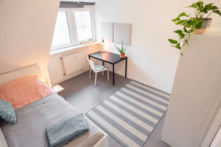 A clean, organized college dorm room with a single bed and desk, highlighting areas to inspect to prevent bed bugs.