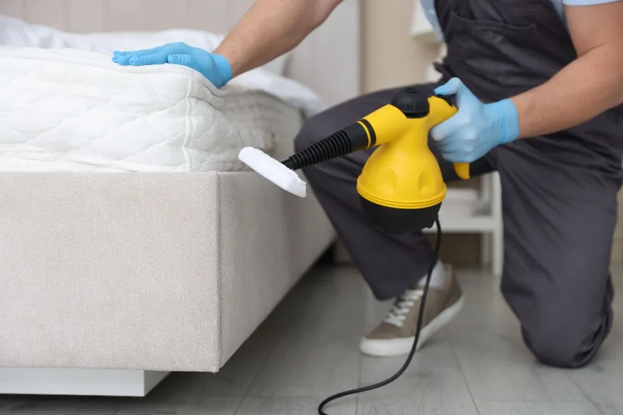 Pest control professional using a handheld steam cleaner on a mattress to kill and prevent bed bugs.